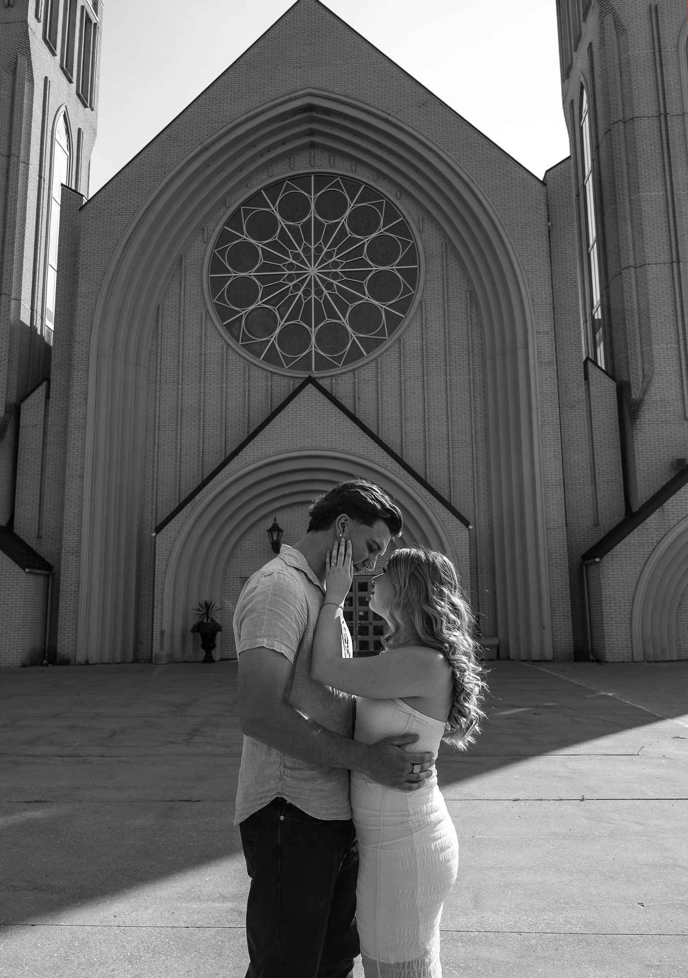 Black and white image of a couple embracing and staring into each other's eyes in front of a church