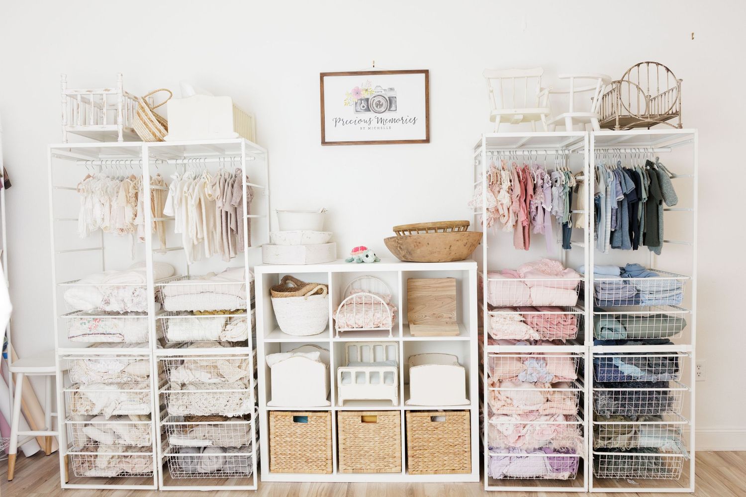 Organized white nursery closet with shelves, baskets, and hanging baby clothes in soft pastel tones.