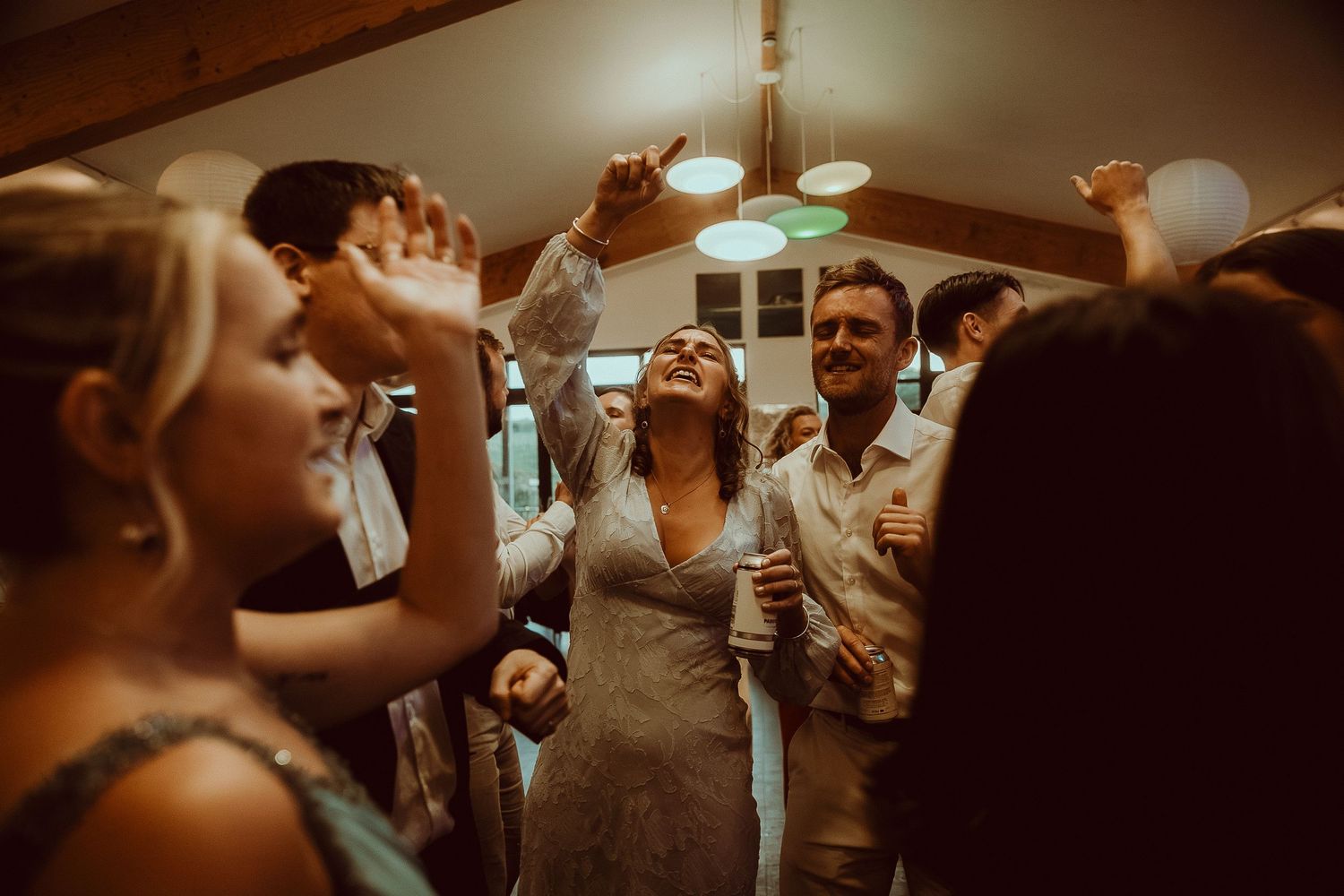 Bride laughing and dancing joyfully with wedding guests in a warmly lit reception venue.