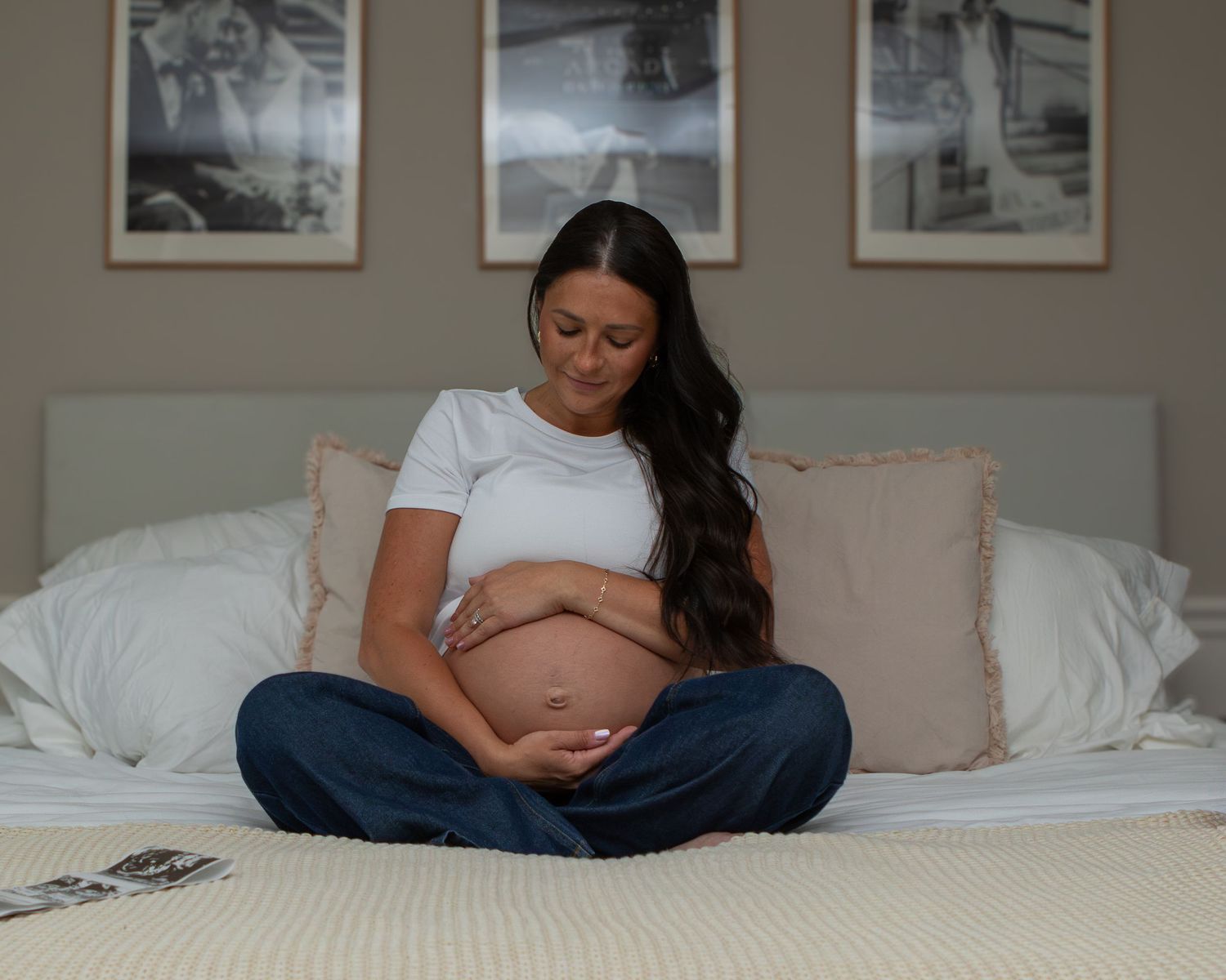 pregnant woman holding belly and smiling sitting on her bed in strongsville