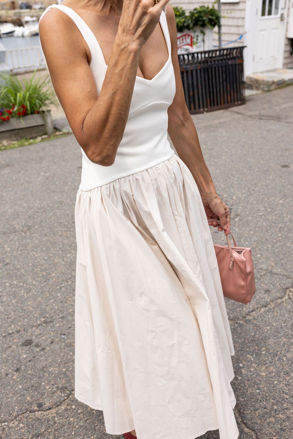 Woman wearing white bodysuit and cream midi skirt holding pink handbag outdoors.
