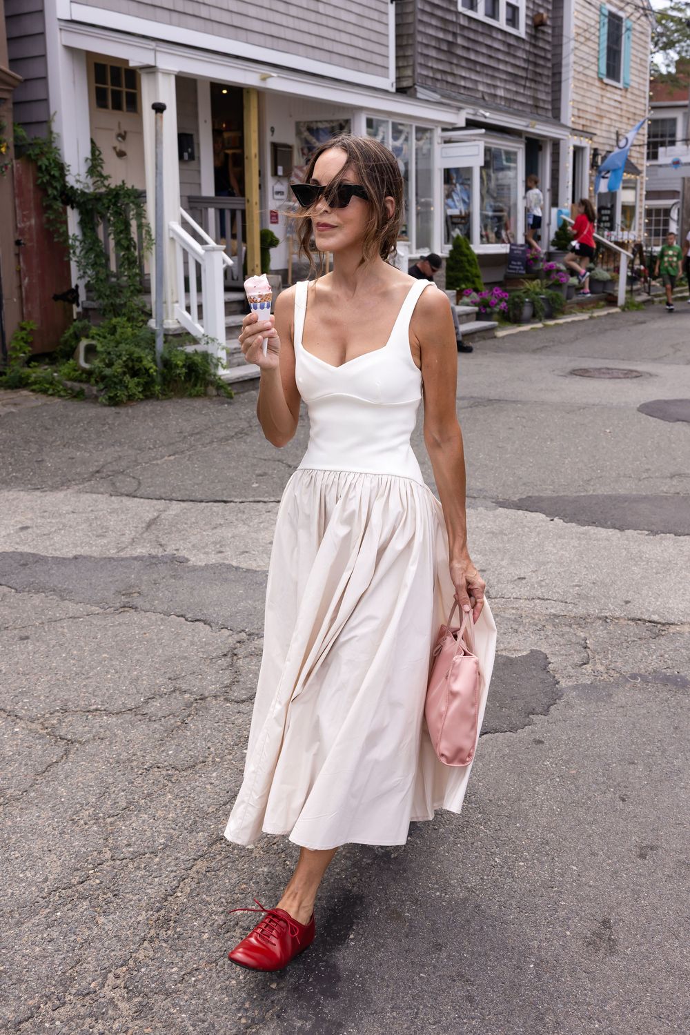Woman in white dress and red mules holding ice cream cone on a charming street.