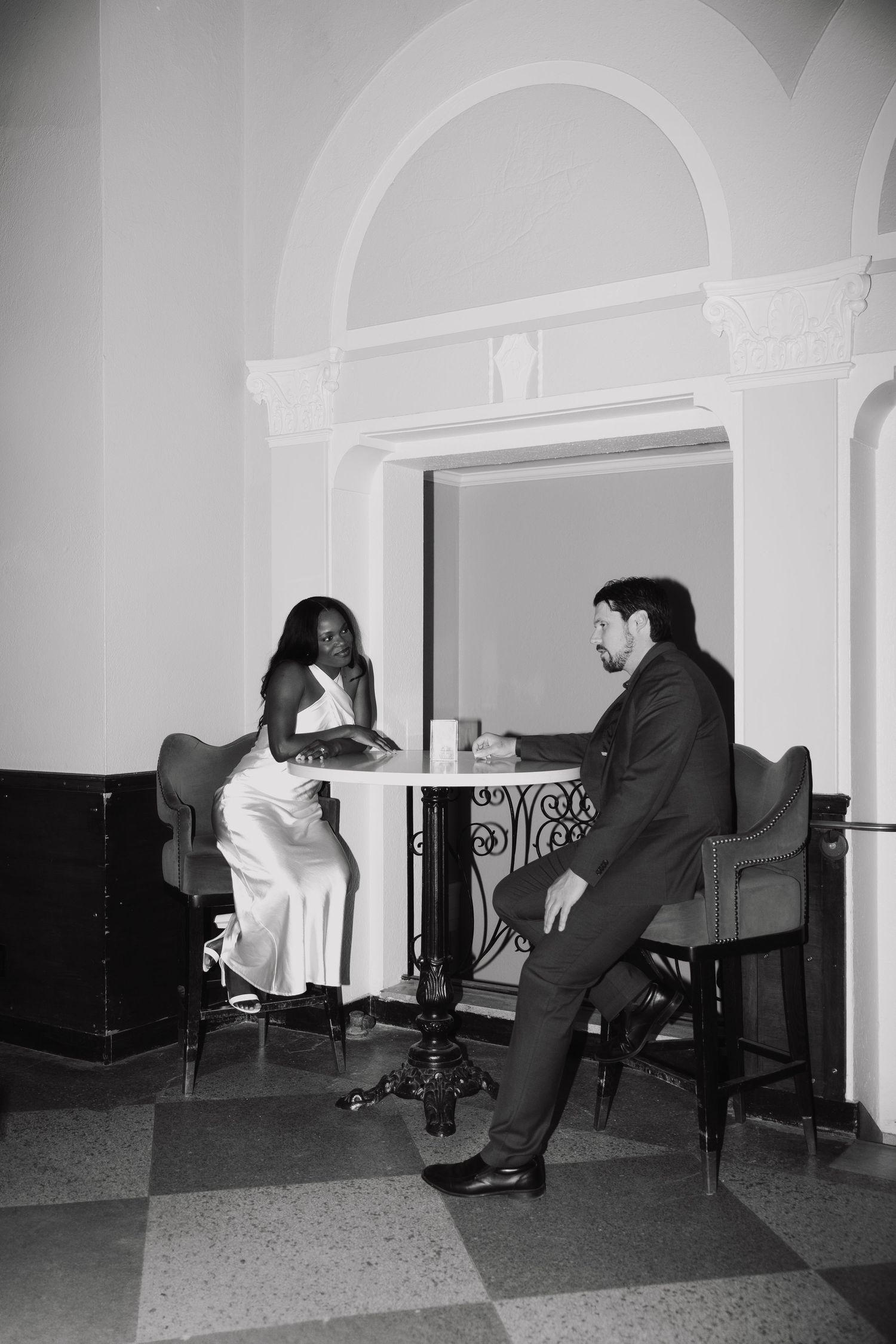 Black and white photo of an interracial couple on a date at an elegant cafe table in a classic interior.