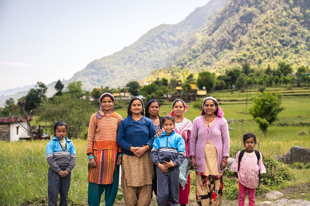 Group of women and children posing outdoors in a lush green mountain village in Nepal.