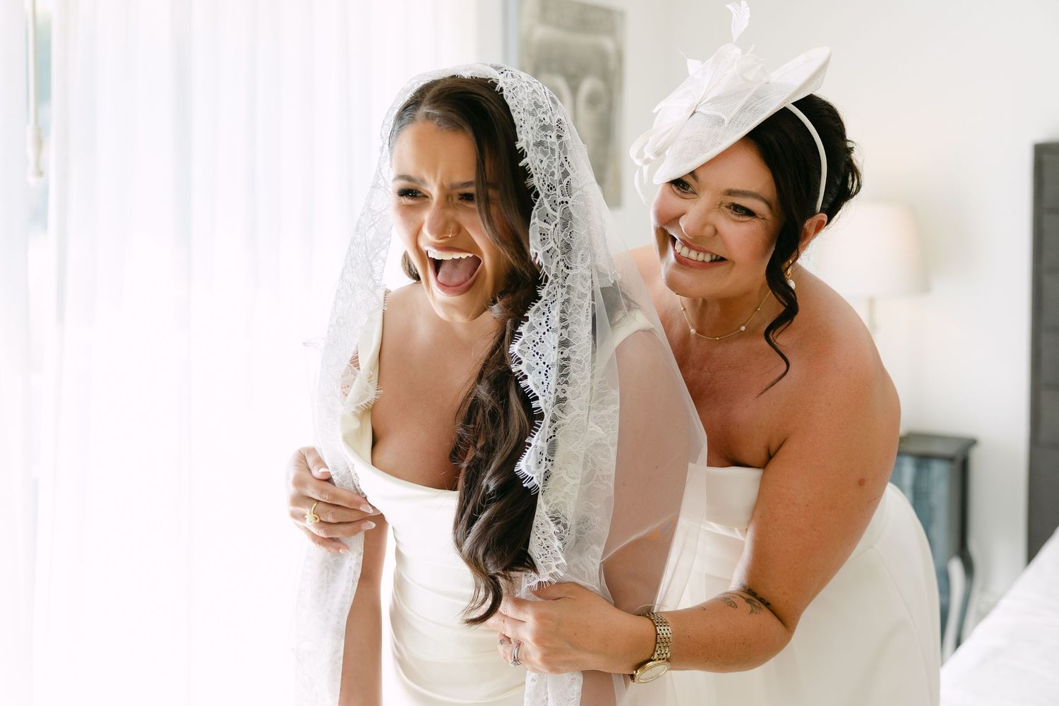 A noiva e a mãe da noiva olham ao espelho e sorriem emocionadas ao verem a noiva pronta