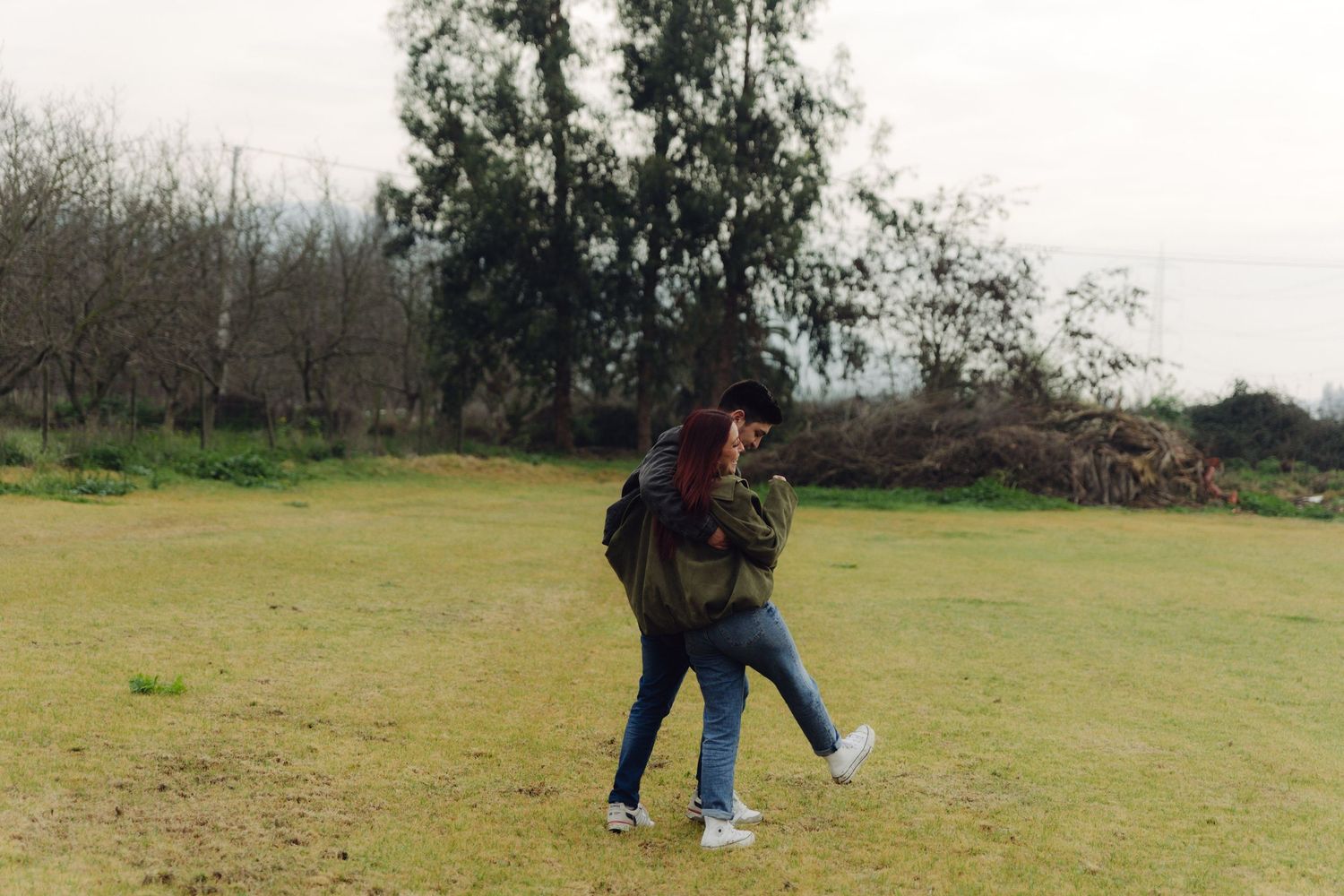 A couple embraces and spins together on a grassy field with trees visible in the background.