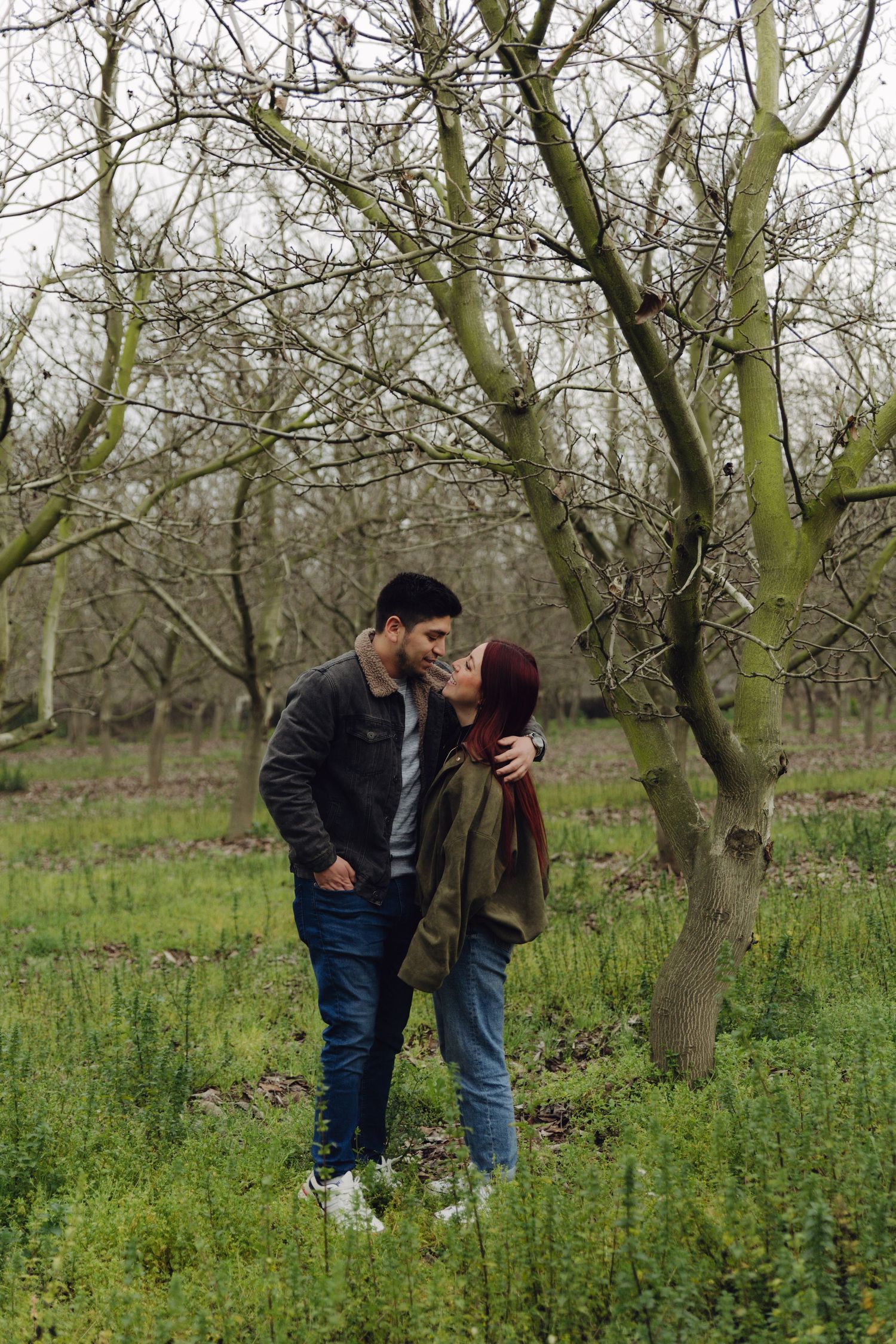 Young couple sharing a romantic moment among leafless trees in a lush green outdoor setting.