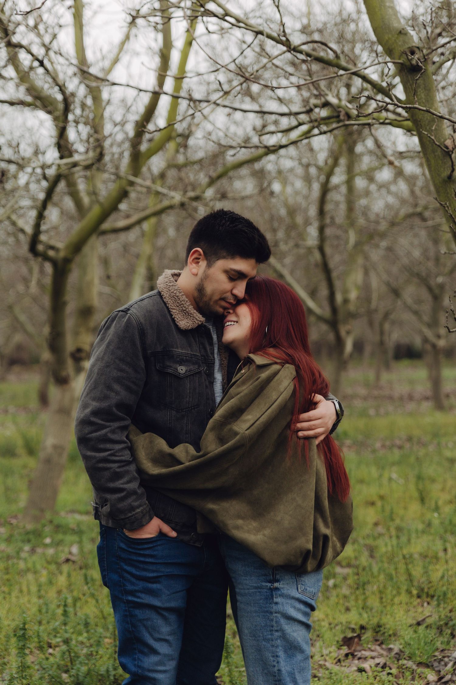 Loving couple cuddling in a serene winter orchard, red-haired woman laughing joyfully.