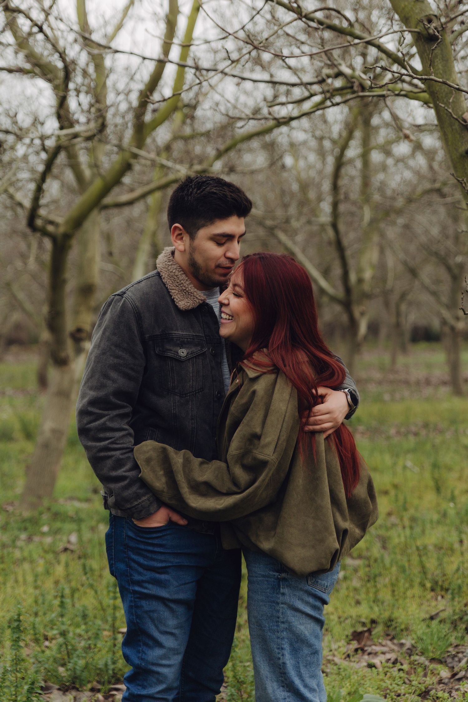Romantic couple hugging in a winter orchard, woman with long red hair smiling warmly.