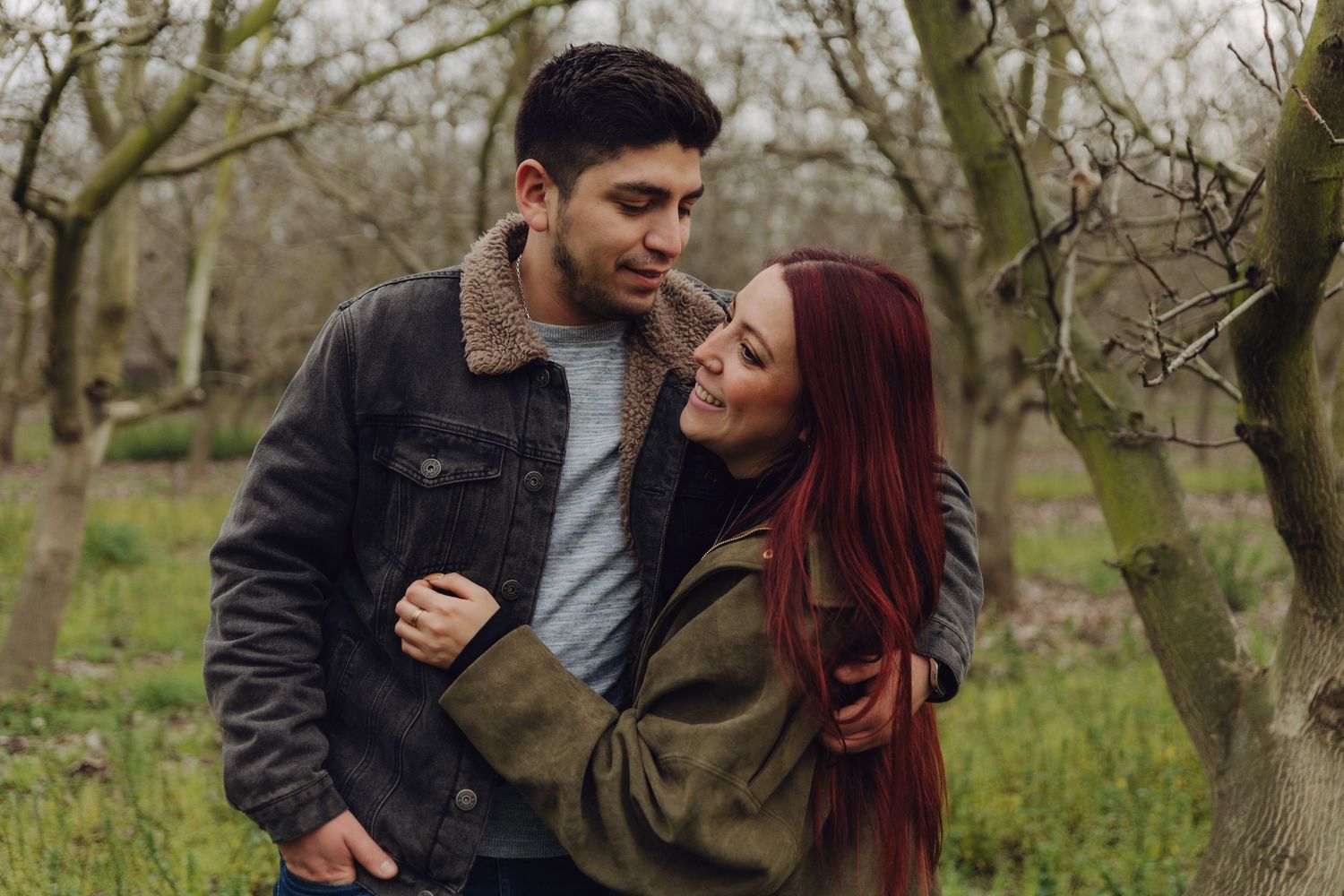 Romantic couple gazing at each other tenderly in a bare winter orchard with green grass.