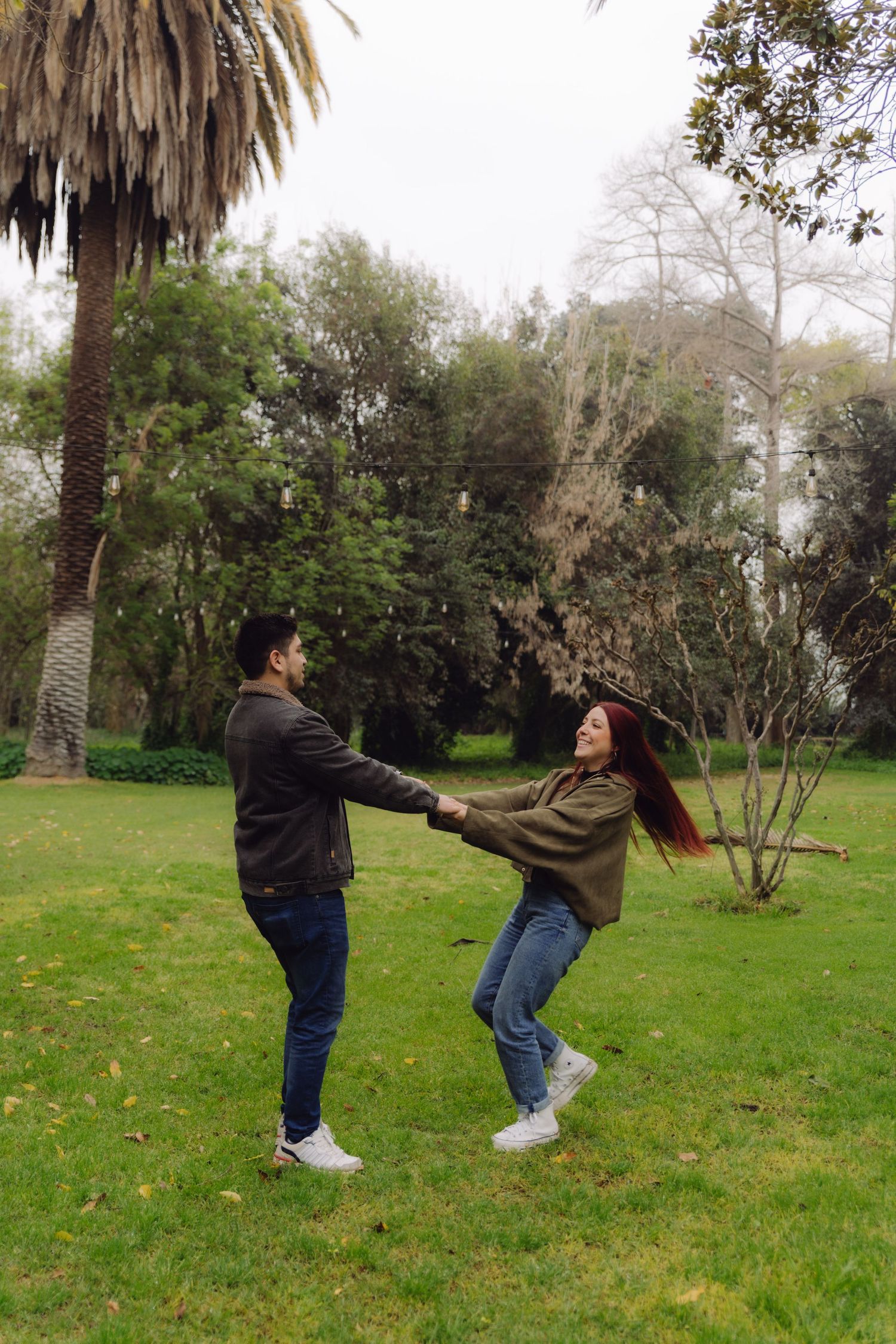 A joyful couple spins together holding hands on a lush green lawn with palm trees behind them.