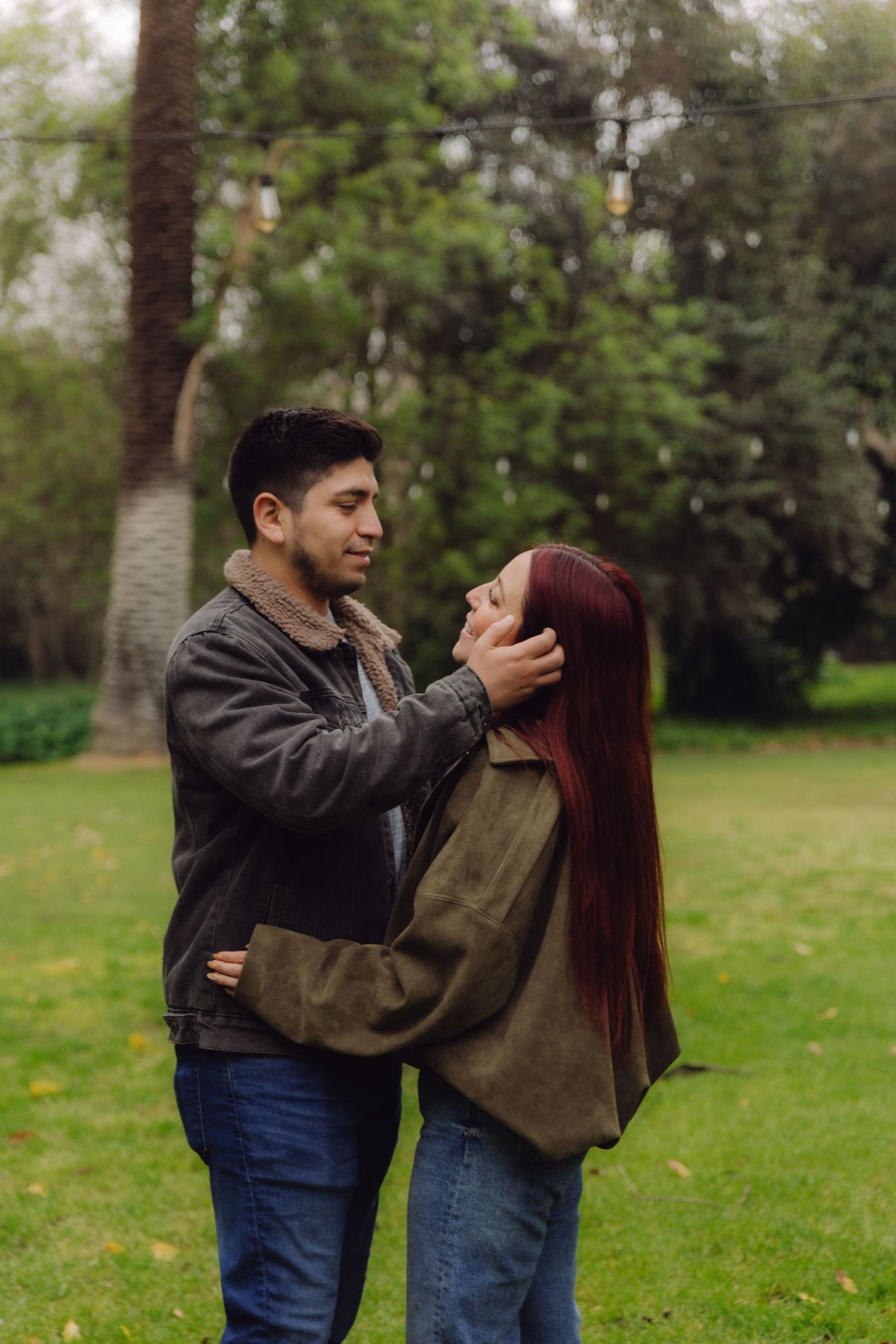 A man tenderly touches a red-haired woman's face as they embrace in a green park setting.