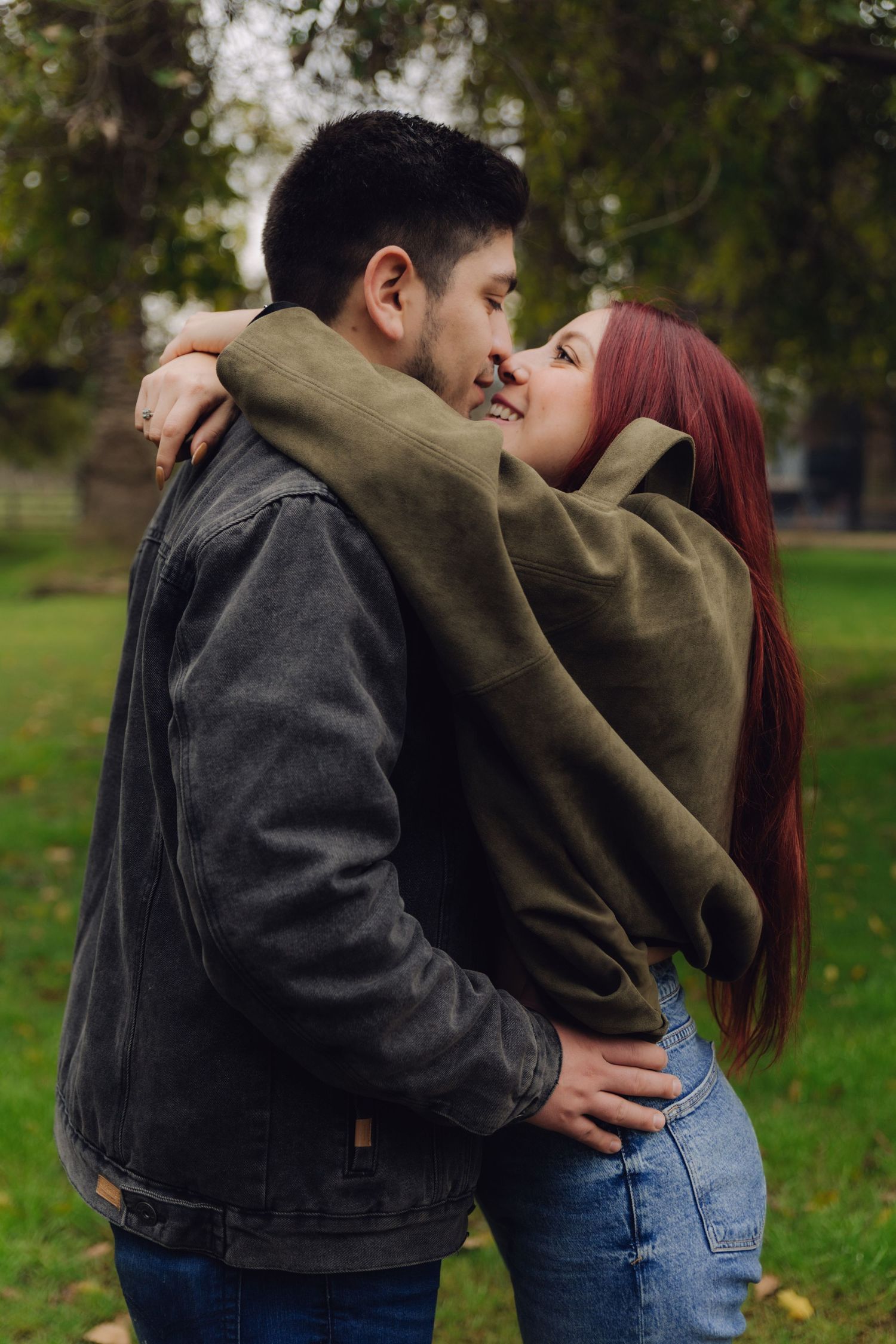 A couple shares a tender almost-kiss moment while embracing outdoors in an autumn park.