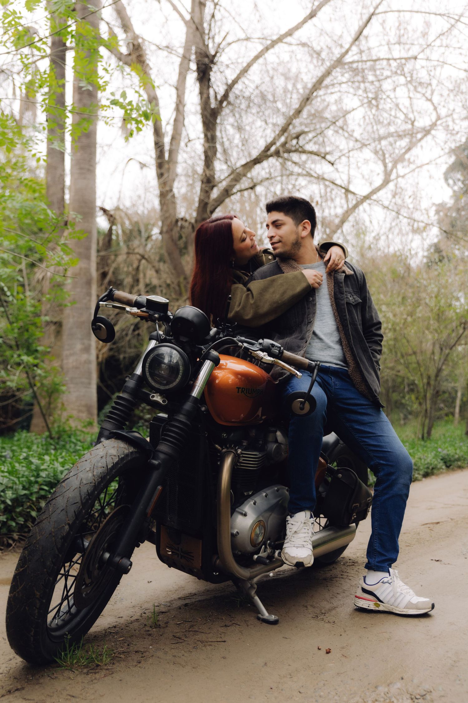 Young couple posing affectionately on a retro orange motorcycle on a forest road.