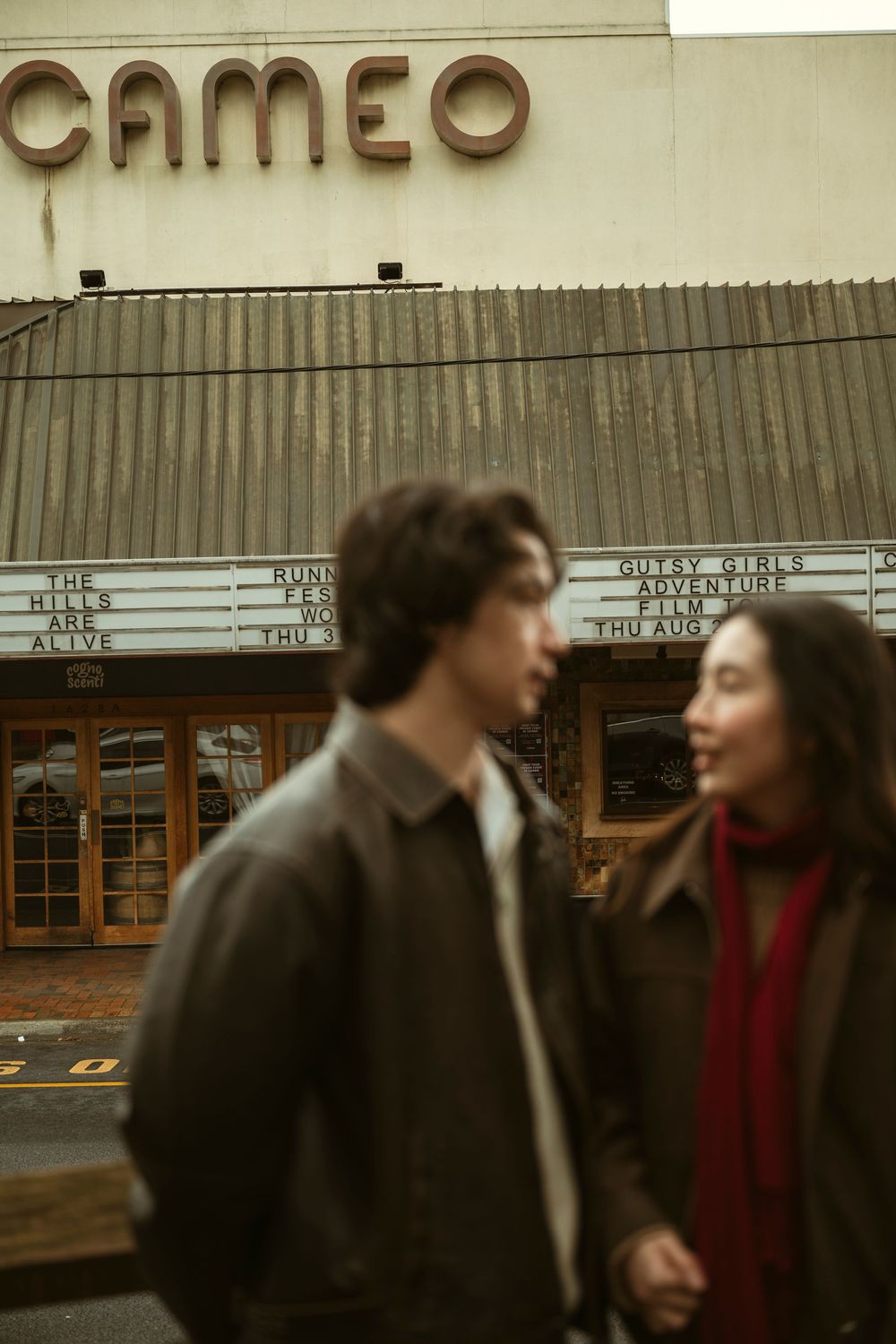 A couple walks hand in hand in front of the vintage Cameo theater marquee on a cloudy day.