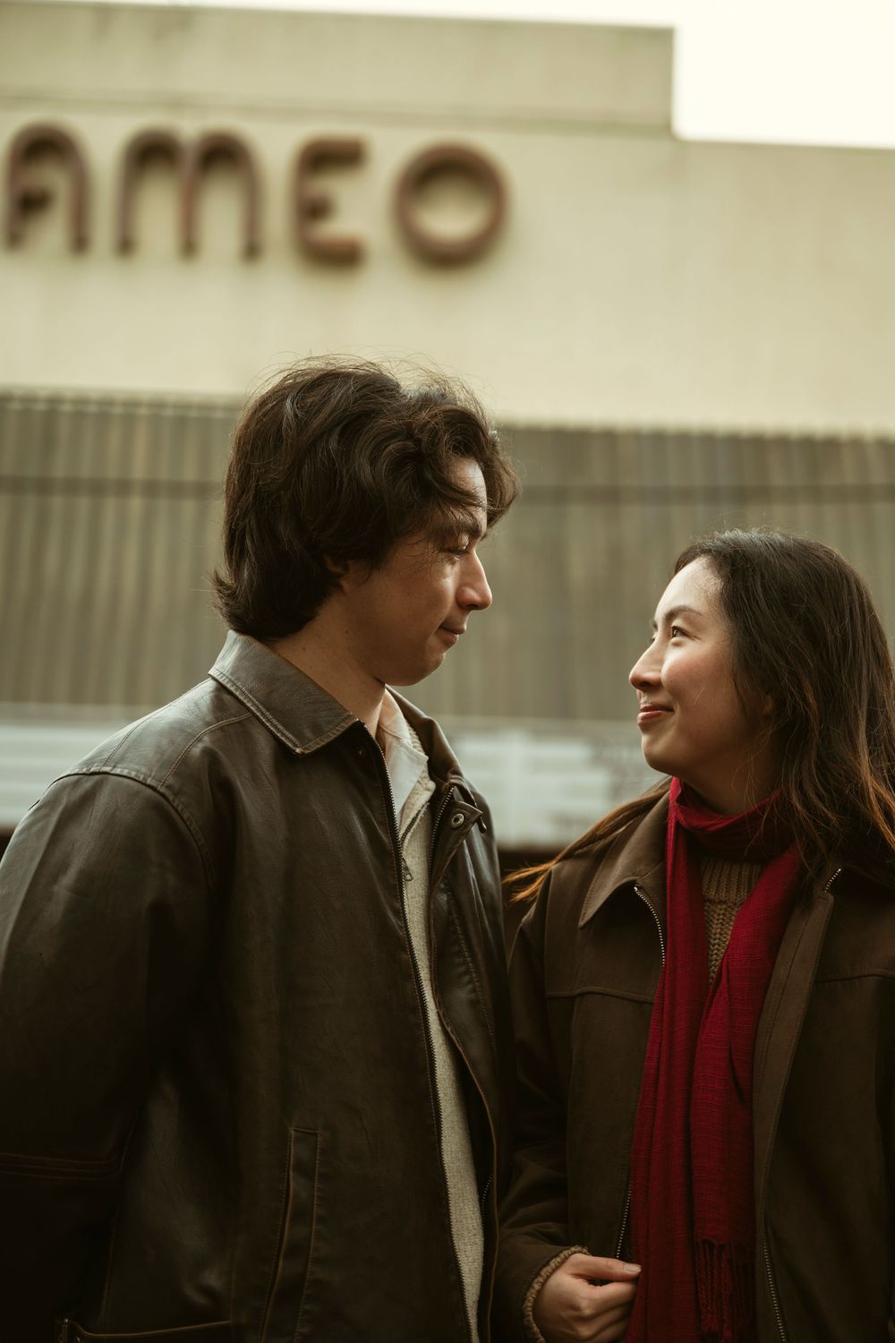 A young couple in leather jackets share a tender moment outside a vintage cinema marquee.