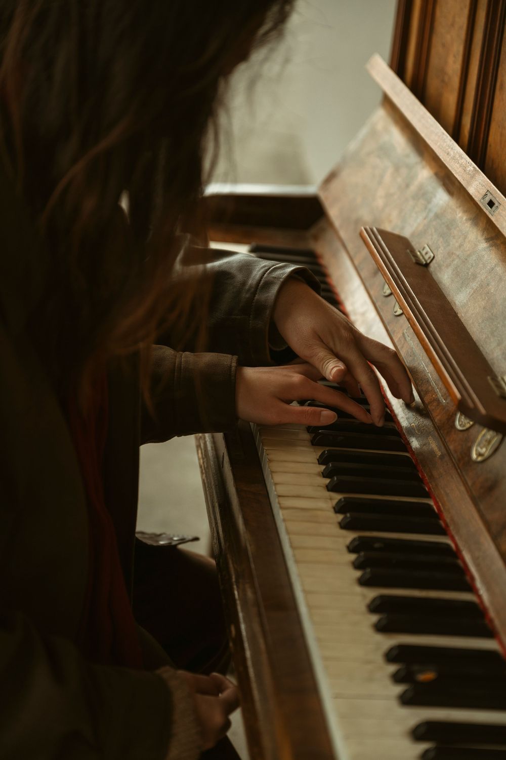 Close-up of a person with long hair playing an antique upright piano, hands on black and white keys.