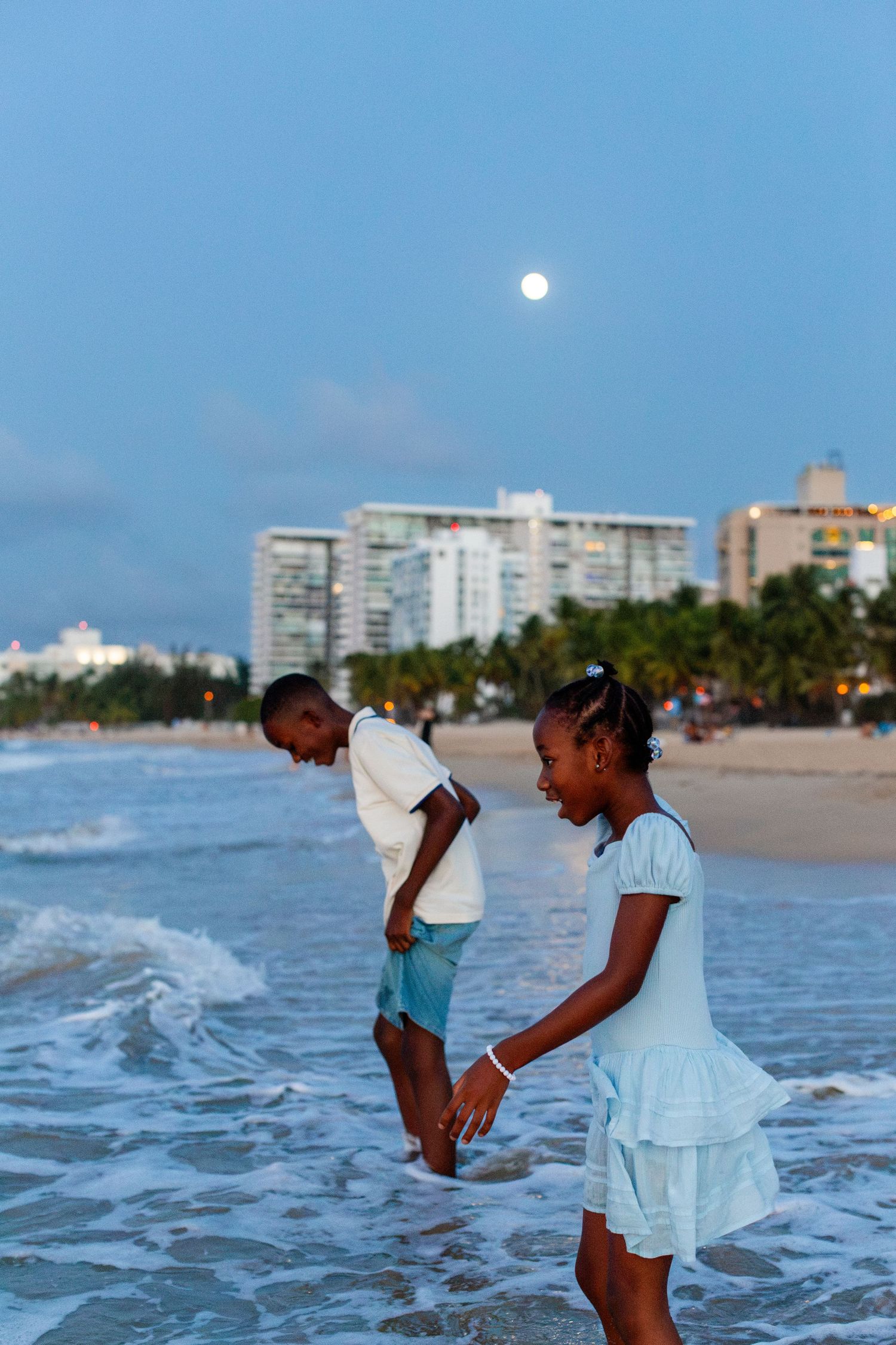Picture of two kids wading in the ocean with the moon in the background at the beach in Isla Verde, Carolina, Puerto Rico.