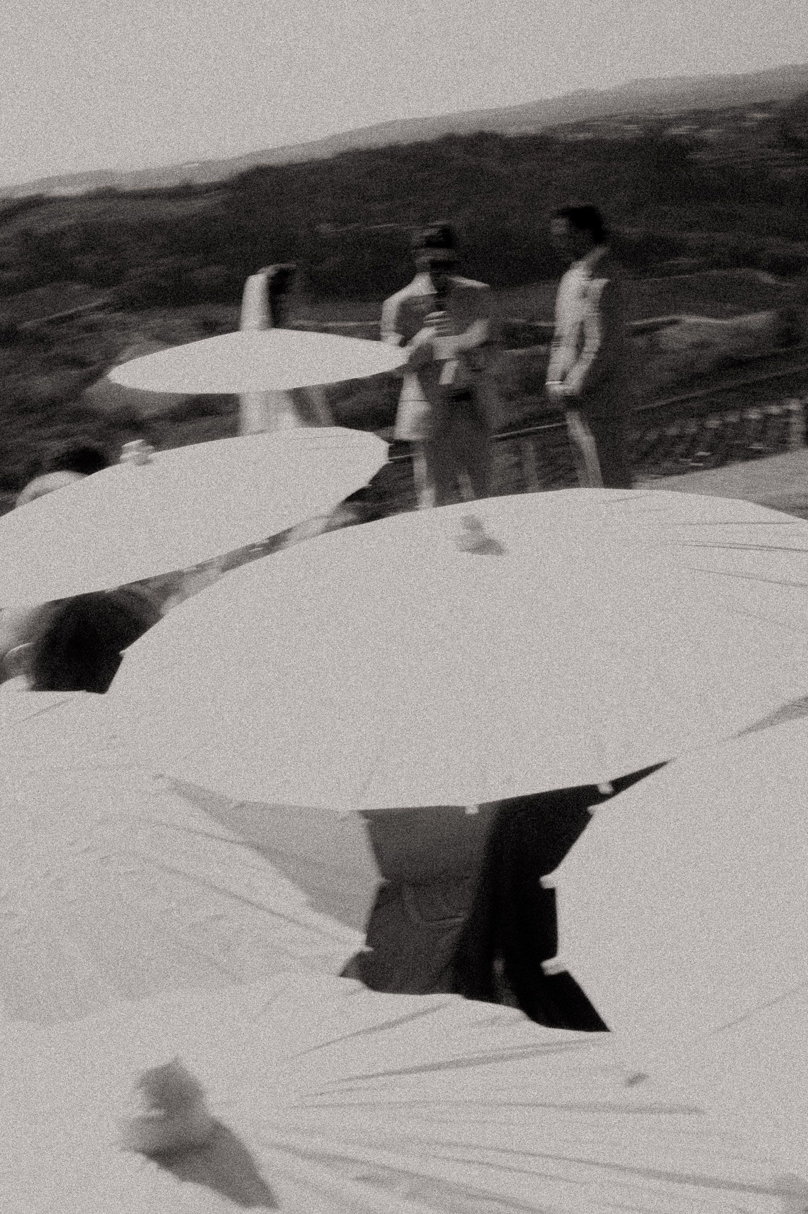 Black and white photo of people gathered on a rooftop terrace surrounded by large white umbrellas and tables.