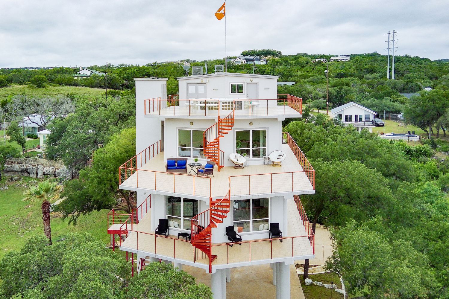 Aerial view of a multi-story white tower home with red spiral staircase surrounded by lush green trees.