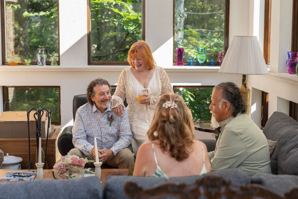 Four adults socializing in a cozy living room, with a woman in white holding a drink while conversing with seated guests.