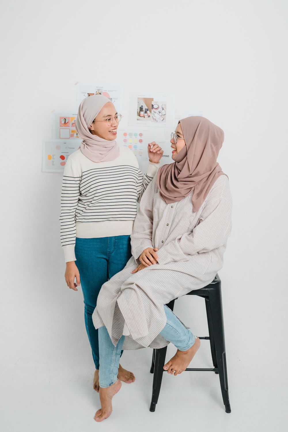 Two people in casual wear and hijabs chat while sitting on chairs.