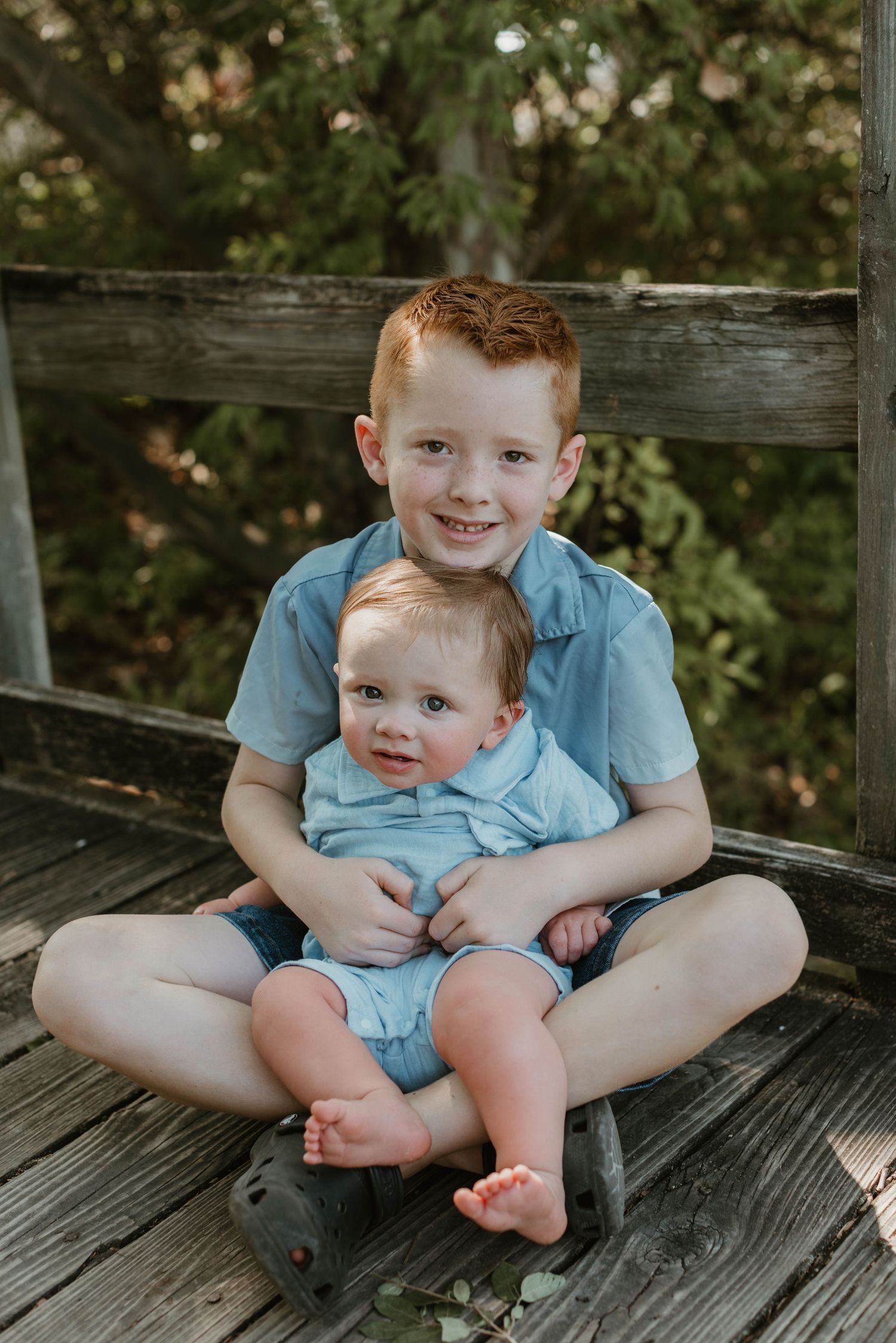 Two children sitting together on wooden deck sharing sweet sibling moment.