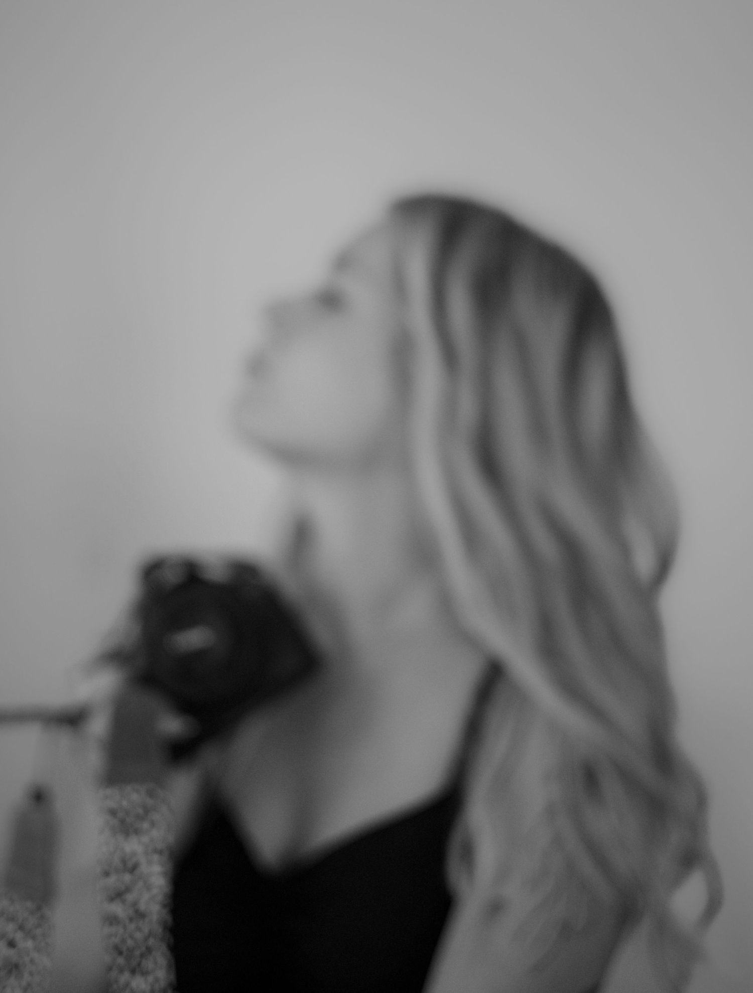Black and white portrait of a blonde woman looking up, holding a camera, artistic blurred photography style.
