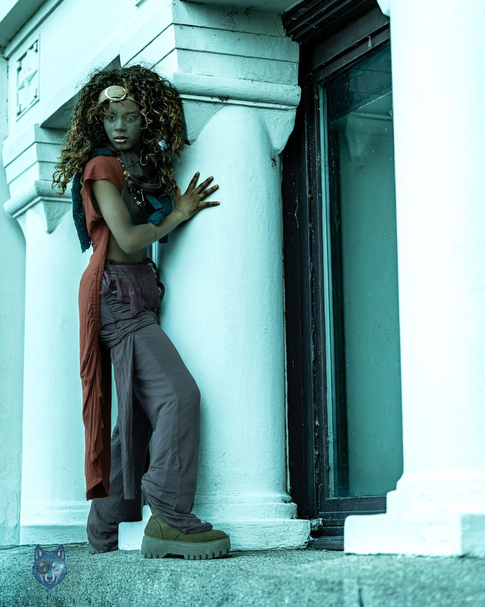 Woman in bohemian costume posing dramatically against a white column in an artistic outdoor photoshoot.