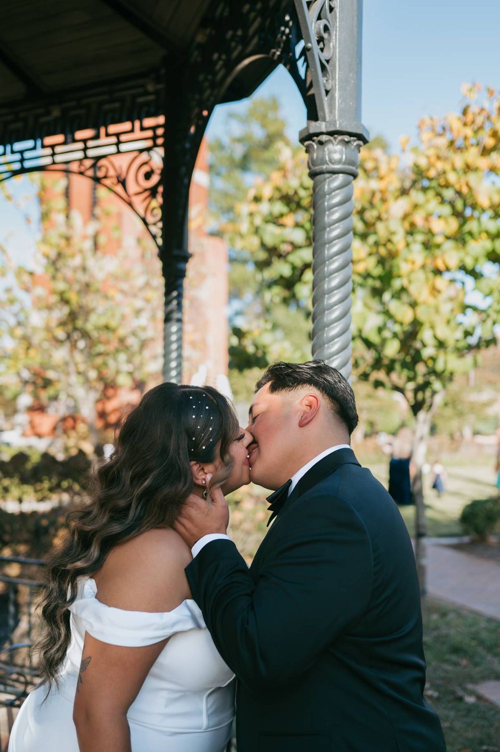 Newlyweds share a tender kiss under decorative iron gazebo on their wedding day, wedding photographer North Carolina