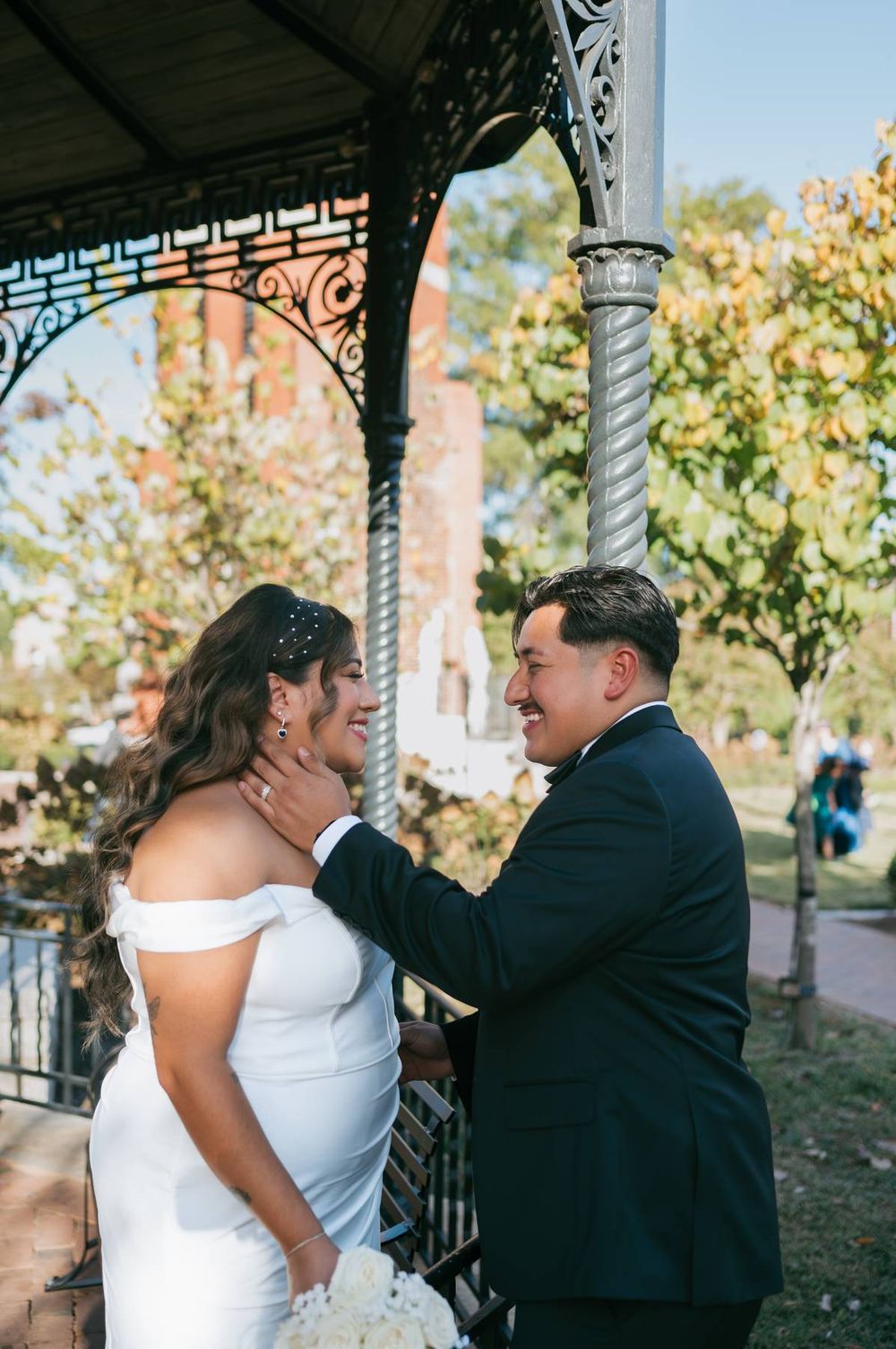 Groom tenderly cups brides face as they share a joyful moment under iron gazebo, wedding photographer Lexington NC