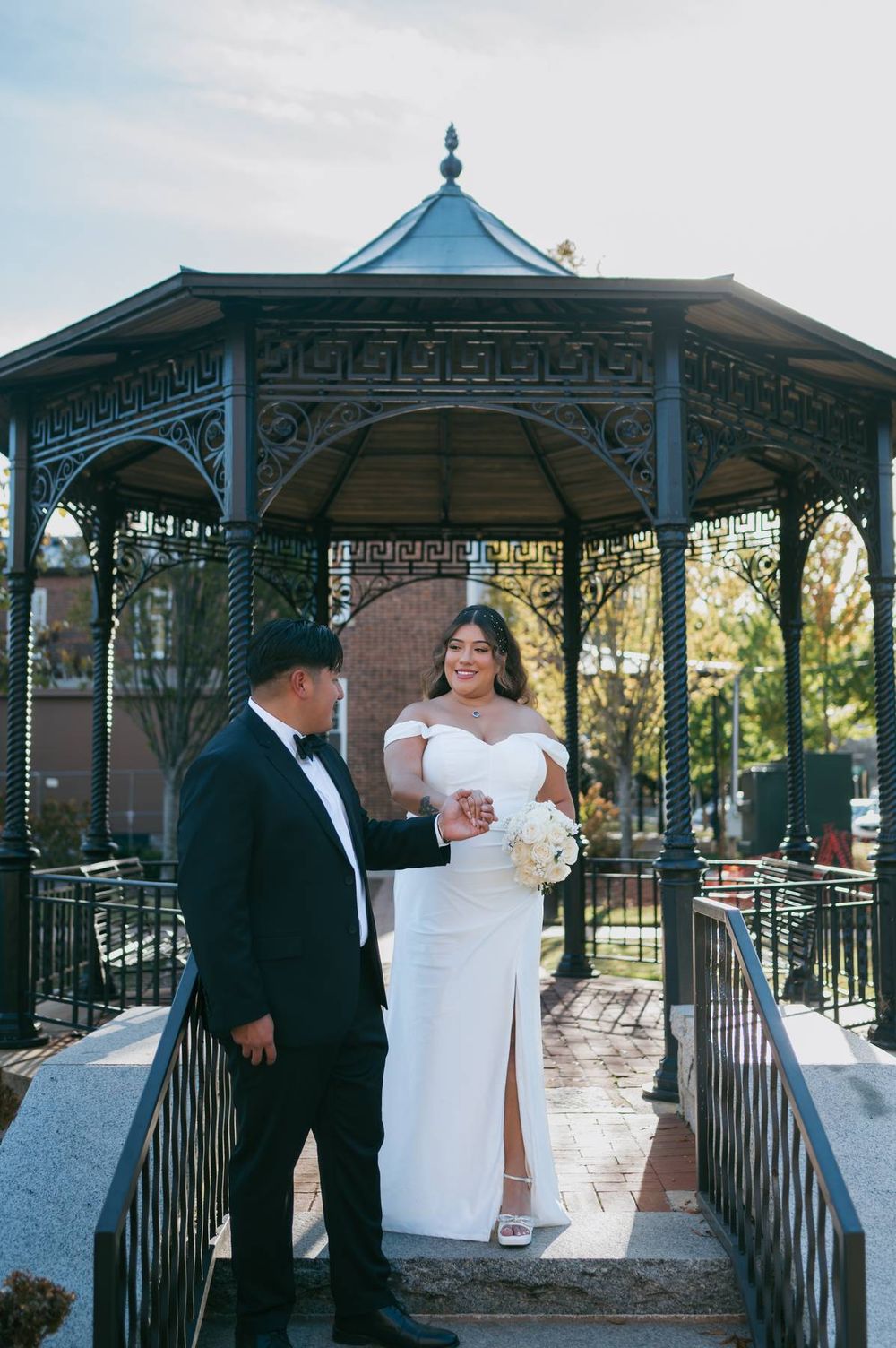 Bride in white gown and groom in tuxedo share romantic moment at ornate iron gazebo, wedding photographer High Point NC