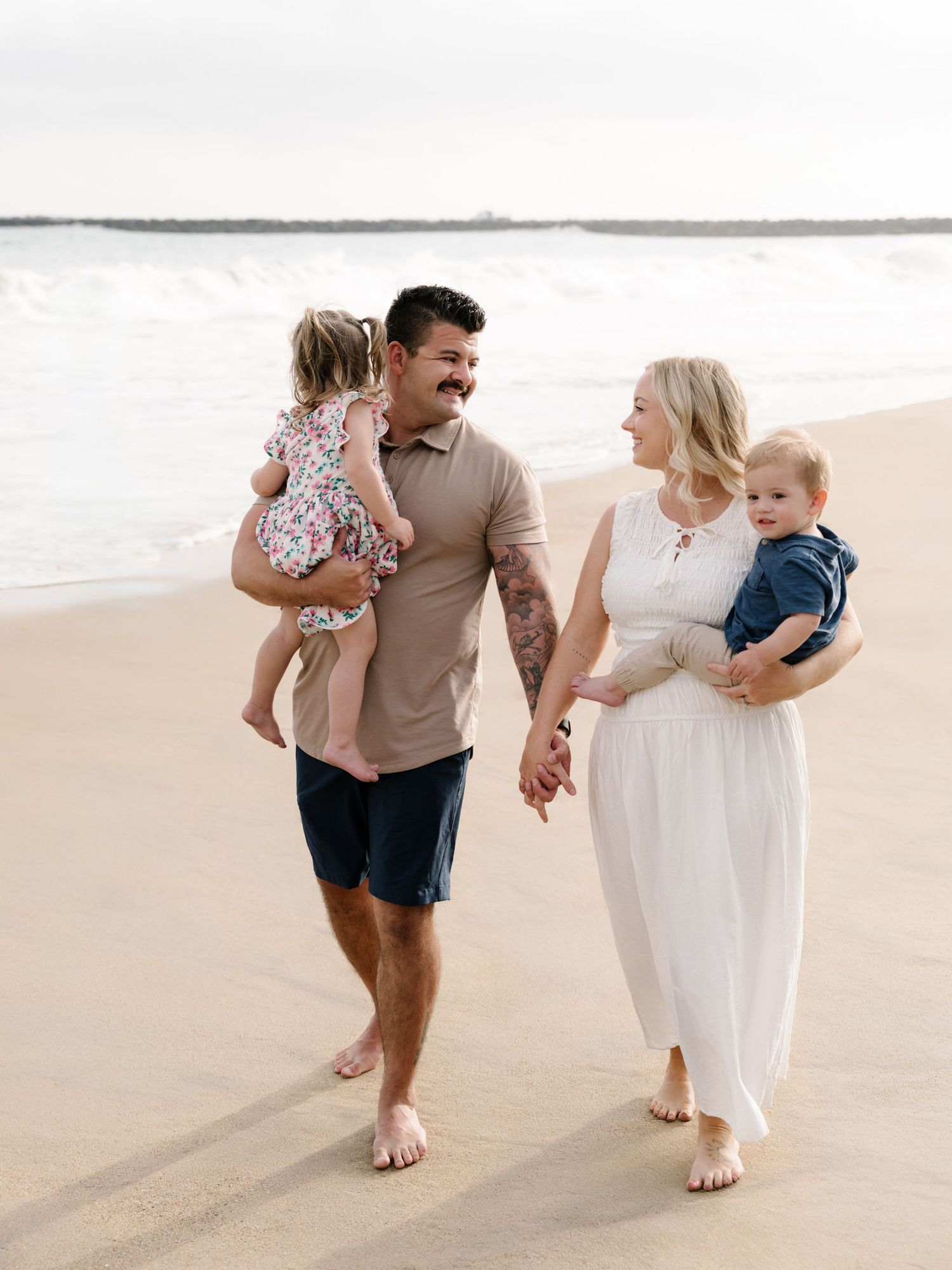 Parents walking hand in hand with young children along the Newport Beach shoreline during an extended family photo session.