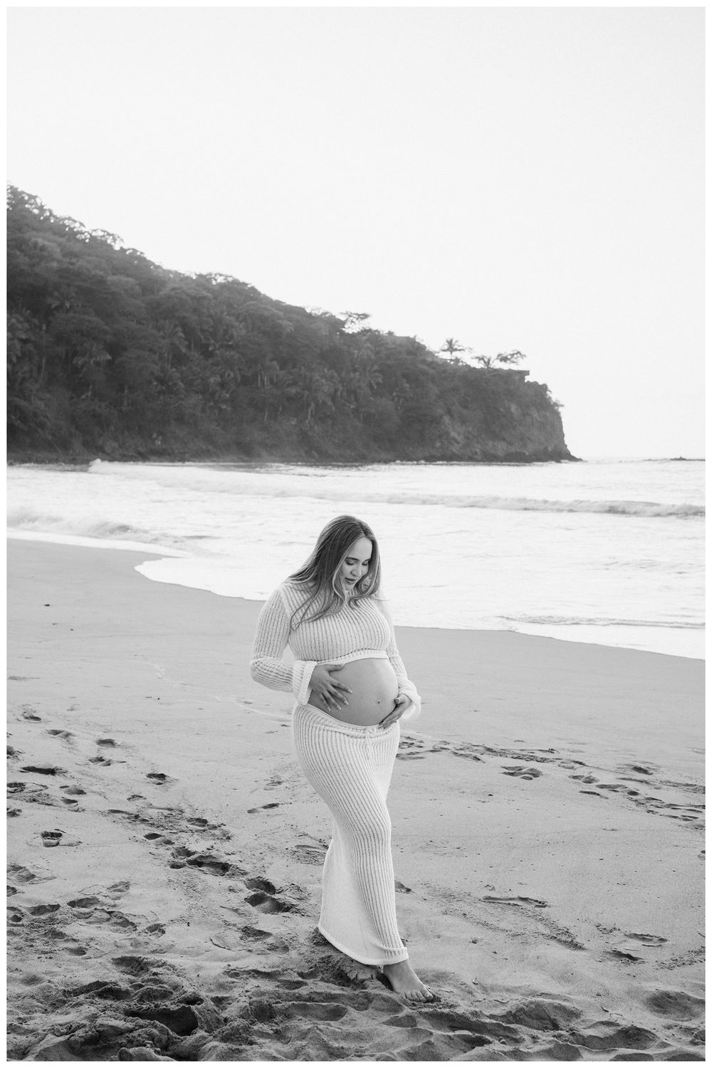 One & Only Mandarina family photographer capturing maternity photos of an expecting mother walking along a peaceful beach.