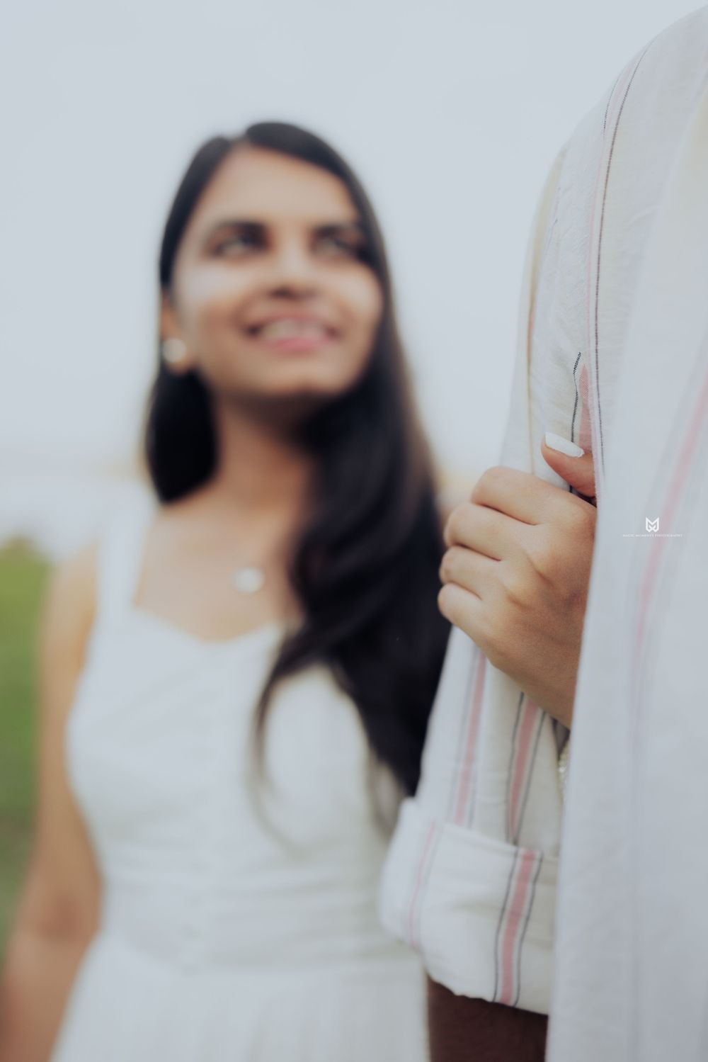Smiling woman in white dress holding man's striped shirt sleeve during romantic outdoor photo session.