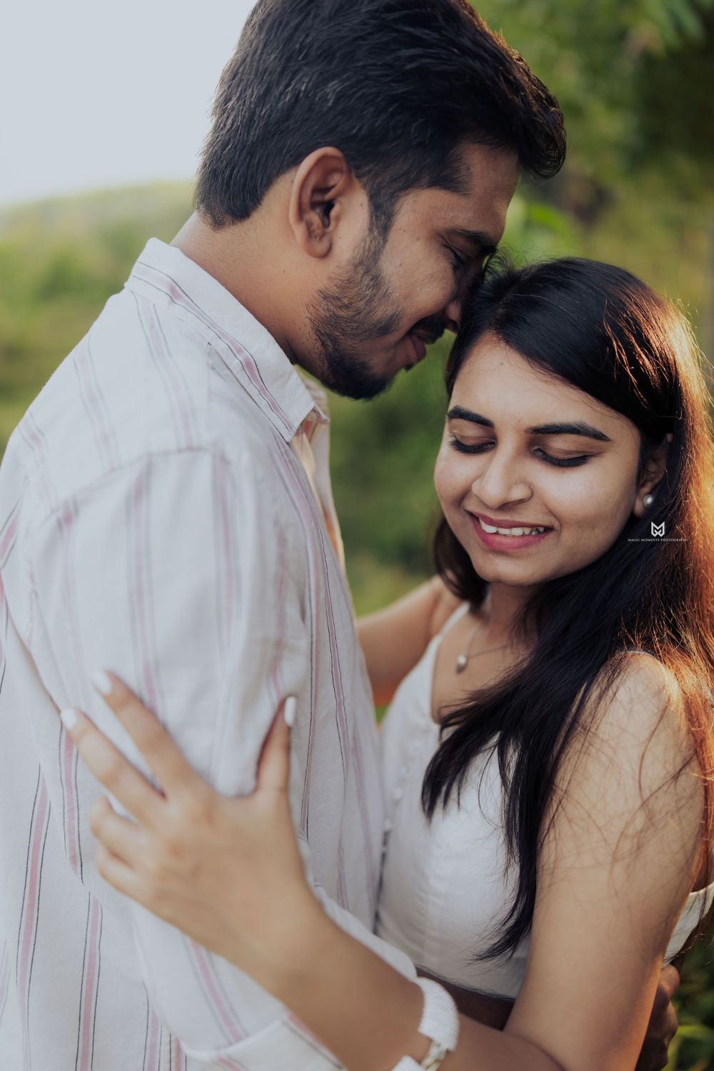 A young couple sharing a romantic embrace outdoors, smiling with foreheads touching in a tender moment.