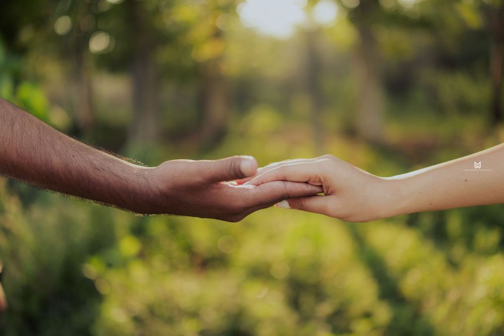 Two people gently holding hands outdoors with a lush green bokeh background, symbolizing love and connection.
