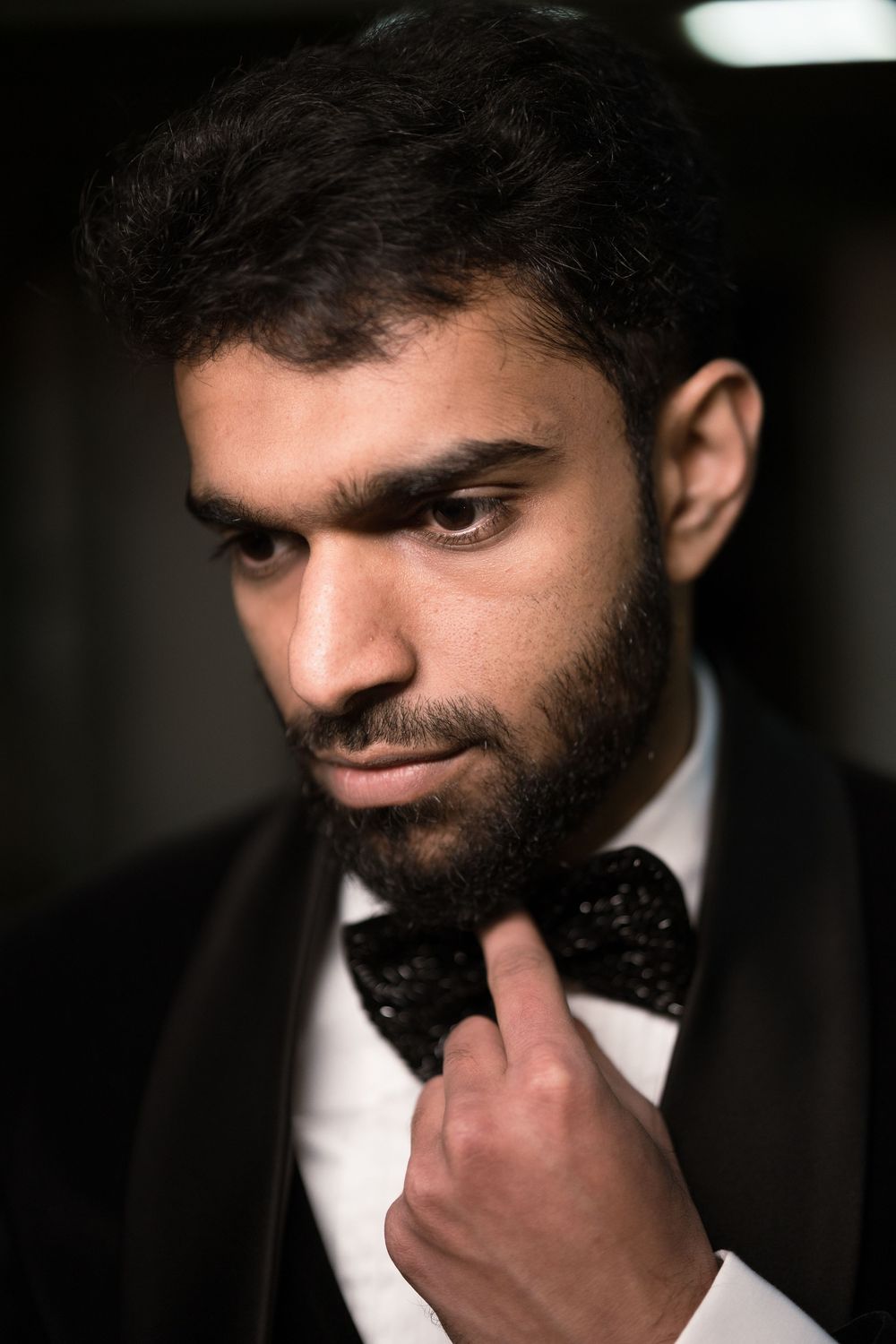 A well-dressed man in a black tuxedo adjusts his bow tie, exuding confidence and elegance.