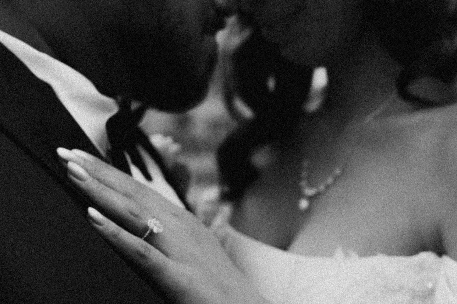 Black and white photo of a bride in a ballgown and veil standing by a window, her reflection visible in a mirror.