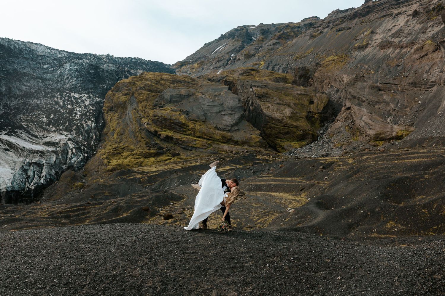 groom dipping his bride at Thórsmörk, Iceland with mountains and a glacier behind them