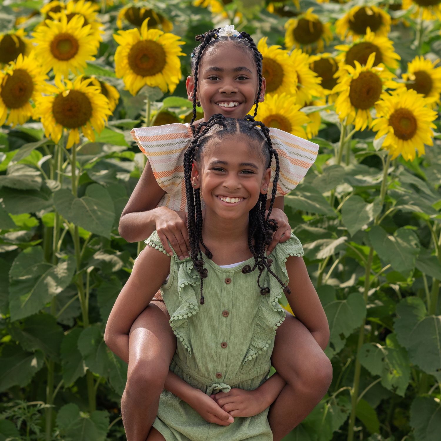 Two young girls smile in a sunflower field for sunflower mini sessions