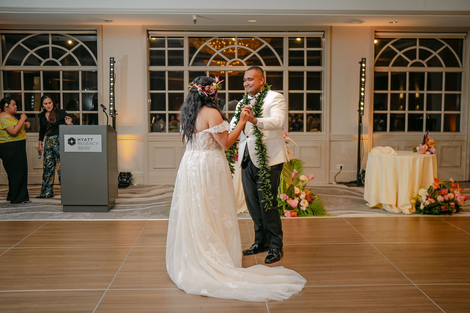 Bride and groom share their first dance at an elegant wedding reception venue with large windows and warm lighting.