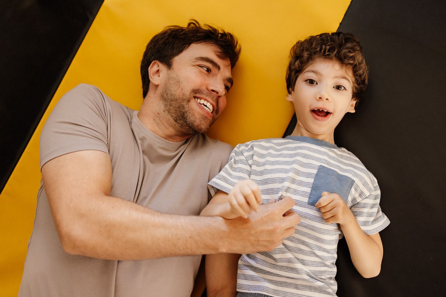A father and young son lie on a yellow and black surface
