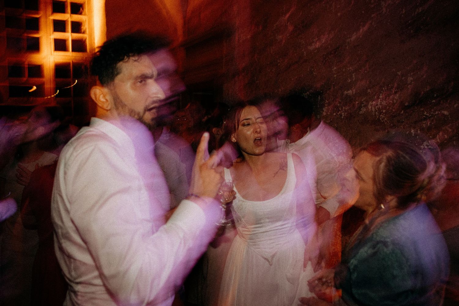 Bride and groom dancing joyfully at wedding reception with motion blur and colorful lighting.