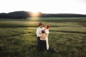 Family embracing at golden sunset in lush green meadow with rolling hills in background.