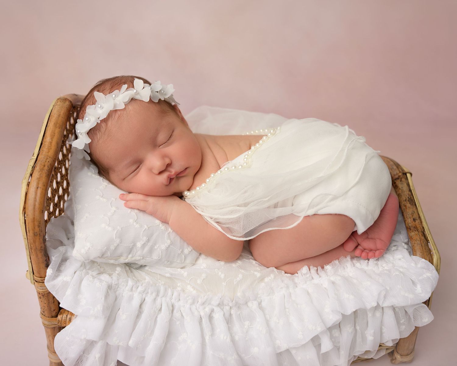 Newborn baby girl in a white wrap and floral headband photographed by a Tampa newborn photographer