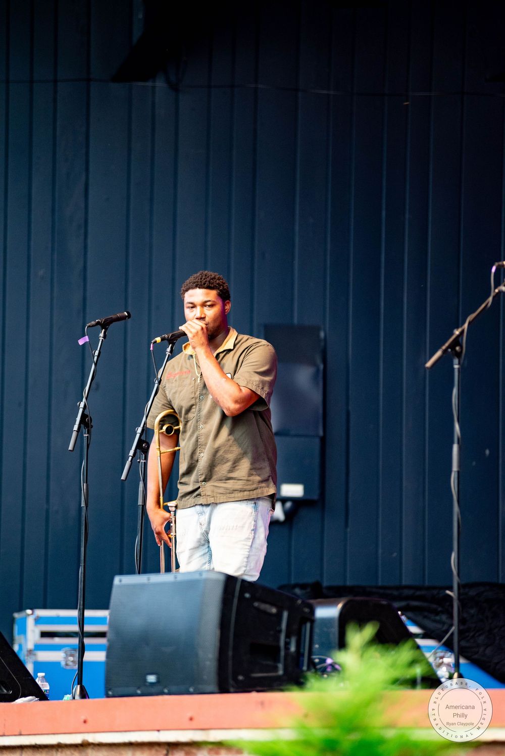 Young man performing on outdoor stage with microphone stand and monitor speakers.