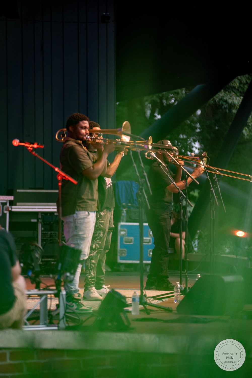 Two musicians playing trombones on an outdoor stage during a live jazz performance.