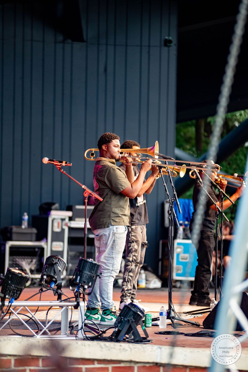 Young musicians play trombones on an outdoor stage during a live performance.