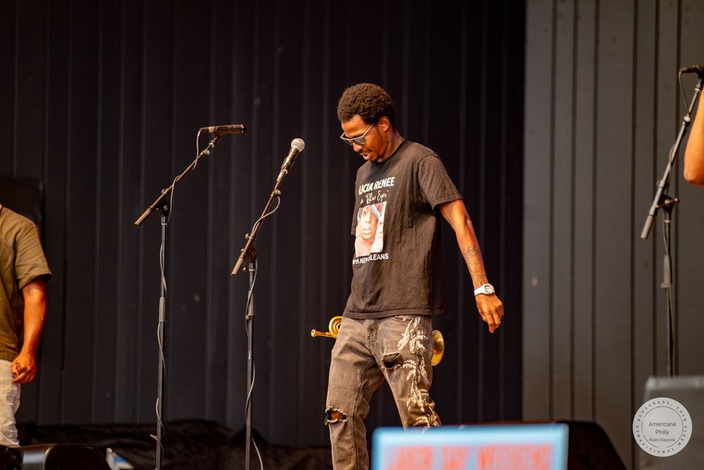 A man in a graphic t-shirt and jeans performs on stage with microphones at a live music event.